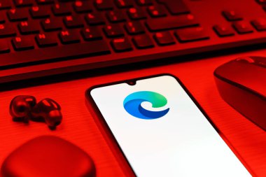 Prag, Çek Cumhuriyeti - 08 12 2025: Kenar logosunu gösteren klavyesi ve cep telefonu olan bir masanın yan görüntüsü. Edge, Microsoft tarafından Windows aygıtları için geliştirilen bir web tarayıcısıdır..