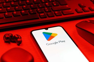 Prag, Çek Cumhuriyeti - 08 12 2025: Google Play logosunu gösteren klavyesi ve cep telefonu olan bir masanın yan görüntüsü. Google Play uygulamaları, oyunları ve dijital içeriği indirmek için bir platformdur.