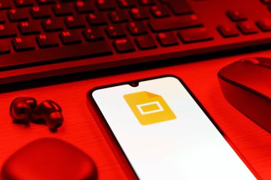 Prag, Çek Cumhuriyeti - 08 12 2025: Google Slides logosunu gösteren klavyesi ve cep telefonu olan bir masanın yan görüntüsü. Google Slides sunumlar ve slayt gösterileri oluşturmak için bir platformdur.