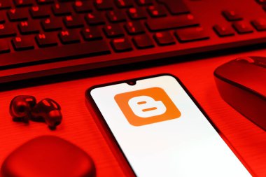 Prag, Çek Cumhuriyeti - 08 12 2025: Blogger logosunu gösteren klavyesi ve cep telefonu olan bir masanın yan görüntüsü. Blogger blog oluşturma ve yayınlama için bir platformdur.
