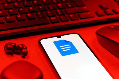 Prag, Çek Cumhuriyeti - 08 12 2025: Google Docs logosunu gösteren klavyesi ve cep telefonu olan bir masanın yan görüntüsü. Google Docs metin belgeleri oluşturmak ve düzenlemek için bir platformdur.