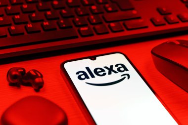 Prag, Çek Cumhuriyeti - 08 12 2025: Alexa logosunu gösteren klavyesi ve cep telefonu olan bir masanın yan görüntüsü. Alexa akıllı aygıtlar ve servisler için ses asistanıdır.