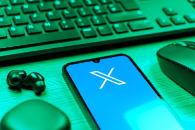 Prague, Czechia - 08 12 2025: A side view of a desk with a keyboard and a mobile phone displaying the X logo. X is a platform for sharing short posts and updates.