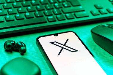 Prague, Czechia - 08 12 2025: A side view of a desk with a keyboard and a mobile phone displaying the X logo. X is a platform for sharing short posts and updates.