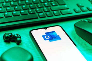 Prague, Czechia - 08 12 2025: A side view of a desk with a keyboard and a mobile phone displaying the Outlook logo. Outlook is an email platform for sending and managing messages.