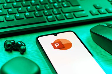Prague, Czechia - 08 12 2025: A side view of a desk with a keyboard and a mobile phone displaying the Powerpoint logo. Powerpoint is a software for creating presentations and slideshows.