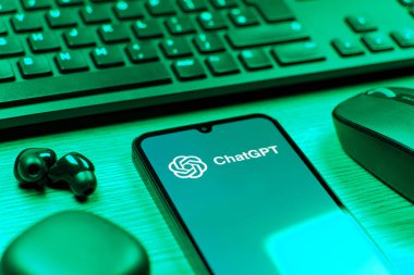 Prague, Czechia - 08 12 2025: A side view of a desk with a keyboard and a mobile phone displaying the ChatGPT logo. ChatGPT is an AI chatbot for generating text and answering questions.