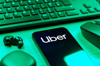 Prag, Çek Cumhuriyeti - 08 12 2025: Uber logosunu gösteren klavyesi ve cep telefonu olan bir masanın yan görüntüsü. Uber ulaşım ve dağıtım hizmetleri için bir gezinti selamlama uygulaması.