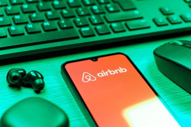 Prag, Çek Cumhuriyeti - 08 12 2025: Airbnb logosunu gösteren klavyesi ve cep telefonu olan bir masanın yan görüntüsü. Airbnb dünya çapında kısa vadeli konaklama için bir platformdur..