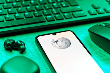 Prag, Çek Cumhuriyeti - 08 12 2025: Vikipedi logosunu gösteren klavyesi ve cep telefonu olan bir masanın yan görüntüsü. Vikipedi çevrimiçi bir ansiklopedidir..