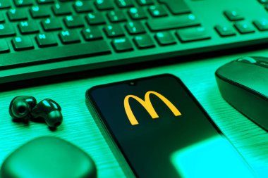 Prag, Çek Cumhuriyeti - 08 12 2025: McDonalds logosunu gösteren klavyesi ve cep telefonu olan bir masanın yan görüntüsü. McDonalds hamburger, patates kızartması ve daha fazlası sunan bir fast-food zinciri..