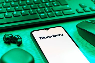 Prag, Çek Cumhuriyeti - 08 12 2025: Bloomberg logosunu gösteren klavyesi ve cep telefonu olan bir masanın yan görüntüsü. Bloomberg finansal haberler, veriler ve analizler sağlayan bir şirkettir..