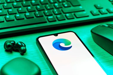 Prag, Çek Cumhuriyeti - 08 12 2025: Kenar logosunu gösteren klavyesi ve cep telefonu olan bir masanın yan görüntüsü. Edge, Microsoft tarafından Windows aygıtları için geliştirilen bir web tarayıcısıdır..
