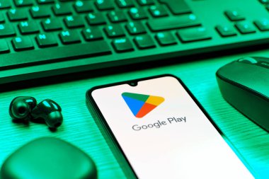 Prag, Çek Cumhuriyeti - 08 12 2025: Google Play logosunu gösteren klavyesi ve cep telefonu olan bir masanın yan görüntüsü. Google Play uygulamaları, oyunları ve dijital içeriği indirmek için bir platformdur.