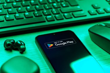 Prag, Çek Cumhuriyeti - 08 12 2025: Google Play logosunu gösteren klavyesi ve cep telefonu olan bir masanın yan görüntüsü. Google Play uygulamaları, oyunları ve dijital içeriği indirmek için bir platformdur.