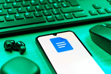 Prag, Çek Cumhuriyeti - 08 12 2025: Google Docs logosunu gösteren klavyesi ve cep telefonu olan bir masanın yan görüntüsü. Google Docs metin belgeleri oluşturmak ve düzenlemek için bir platformdur.