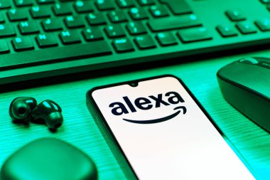 Prag, Çek Cumhuriyeti - 08 12 2025: Alexa logosunu gösteren klavyesi ve cep telefonu olan bir masanın yan görüntüsü. Alexa akıllı aygıtlar ve servisler için ses asistanıdır.