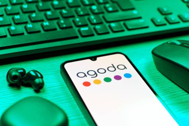 Prag, Çek Cumhuriyeti - 08 12 2025: Agoda logosunu gösteren klavyesi ve cep telefonu olan bir masanın yan görüntüsü. Agoda, otelleri ve seyahat yerlerini ayırtmak için bir platform..