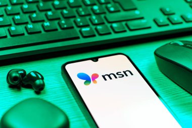Prag, Çek Cumhuriyeti - 08 12 2025: MSN logosunu gösteren klavyesi ve cep telefonu olan bir masanın yan görüntüsü. MSN haber, e-posta ve çevrimiçi hizmetler için bir platformdur.