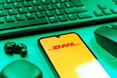 Prag, Çek Cumhuriyeti - 08 12 2025: DHL logosunu gösteren klavyesi ve cep telefonu olan bir masanın yan görüntüsü. DHL uluslararası nakliye hizmeti sunan bir lojistik şirketidir..