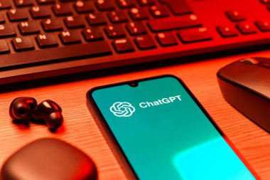 Prague, Czechia - 08 12 2025: A side view of a desk with a keyboard and a mobile phone displaying the ChatGPT logo. ChatGPT is an AI chatbot for generating text and answering questions.