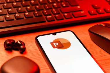 Prague, Czechia - 08 12 2025: A side view of a desk with a keyboard and a mobile phone displaying the Powerpoint logo. Powerpoint is a software for creating presentations and slideshows.