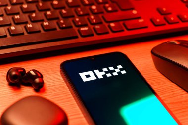 Prague, Czechia - 08 12 2025: A side view of a desk with a keyboard and a mobile phone displaying the OKX logo. OKX is a cryptocurrency exchange for trading digital assets.