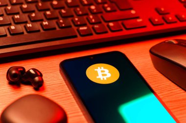 Prag, Çek Cumhuriyeti - 08 12 2025: Bitcoin logosunu gösteren klavyesi ve cep telefonu olan bir masanın yan görüntüsü. Bitcoin merkezi olmayan işlemler için dijital bir kripto para birimidir.