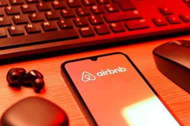 Prag, Çek Cumhuriyeti - 08 12 2025: Airbnb logosunu gösteren klavyesi ve cep telefonu olan bir masanın yan görüntüsü. Airbnb dünya çapında kısa vadeli konaklama için bir platformdur..