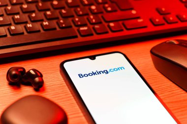 Prag, Çek Cumhuriyeti - 08 12 2025: Booking.com logosunu gösteren klavyesi ve cep telefonu olan bir masanın yan görüntüsü. Rezervasyon, otel bulmak ve rezervasyon yaptırmak için bir platformdur..
