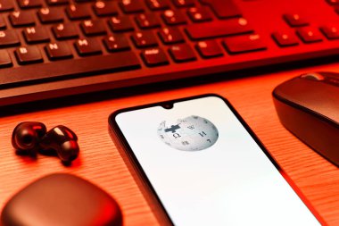 Prag, Çek Cumhuriyeti - 08 12 2025: Vikipedi logosunu gösteren klavyesi ve cep telefonu olan bir masanın yan görüntüsü. Vikipedi çevrimiçi bir ansiklopedidir..