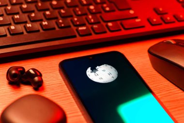 Prag, Çek Cumhuriyeti - 08 12 2025: Vikipedi logosunu gösteren klavyesi ve cep telefonu olan bir masanın yan görüntüsü. Vikipedi çevrimiçi bir ansiklopedidir..