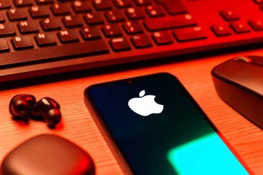 Prag, Çek Cumhuriyeti - 08 12 2025: Apple logosunu gösteren klavyesi ve cep telefonu olan bir masanın yan görüntüsü. Apple iPhone, bilgisayar ve hizmet üreten bir teknoloji şirketidir..