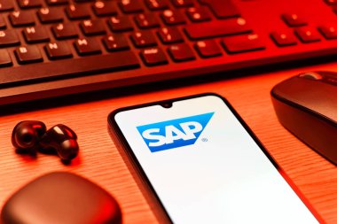 Prag, Çek Cumhuriyeti - 08 12 2025: SAP logosunu gösteren klavyesi ve cep telefonu olan bir masanın yan görüntüsü. SAP, şirket uygulamaları ve çözümleri sağlayan bir yazılım şirketidir..