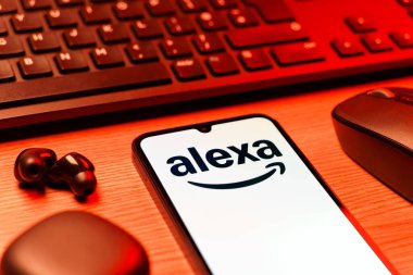 Prag, Çek Cumhuriyeti - 08 12 2025: Alexa logosunu gösteren klavyesi ve cep telefonu olan bir masanın yan görüntüsü. Alexa akıllı aygıtlar ve servisler için ses asistanıdır.