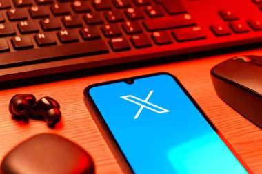Prague, Czechia - 08 12 2025: A side view of a desk with a keyboard and a mobile phone displaying the X logo. X is a platform for sharing short posts and updates.