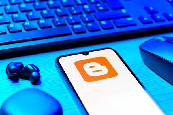 Prag, Çek Cumhuriyeti - 08 12 2025: Blogger logosunu gösteren klavyesi ve cep telefonu olan bir masanın yan görüntüsü. Blogger blog oluşturma ve yayınlama için bir platformdur.