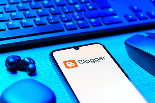 Prag, Çek Cumhuriyeti - 08 12 2025: Blogger logosunu gösteren klavyesi ve cep telefonu olan bir masanın yan görüntüsü. Blogger blog oluşturma ve yayınlama için bir platformdur.