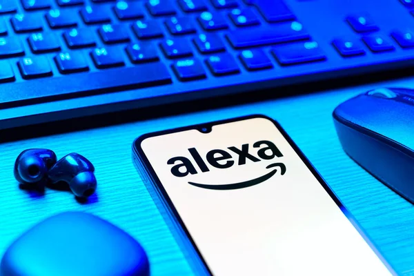 Prag, Çek Cumhuriyeti - 08 12 2025: Alexa logosunu gösteren klavyesi ve cep telefonu olan bir masanın yan görüntüsü. Alexa akıllı aygıtlar ve servisler için ses asistanıdır.