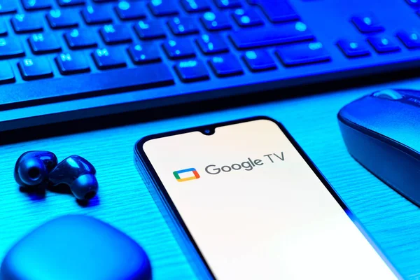 Prag, Çek Cumhuriyeti - 08 12 2025: Google TV logosunu gösteren klavyesi ve cep telefonu olan bir masanın yan görüntüsü. Google TV film, program ve uygulamalar için bir platformdur..