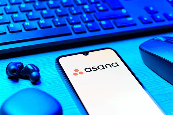 Prag, Çek Cumhuriyeti - 08 12 2025: Asana logosunu gösteren klavyesi ve cep telefonu olan bir masanın yan görüntüsü. Asana görev yönetimi ve takım işbirliği için bir platformdur..