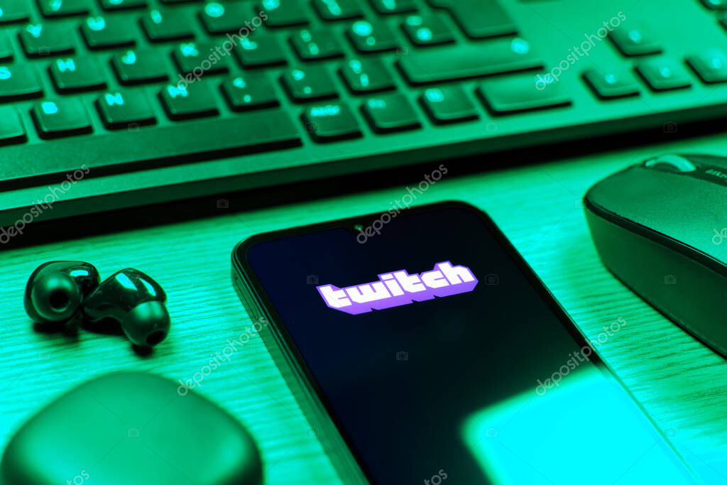 Prague, Czechia - 08 12 2025: A side view of a desk with a keyboard and a mobile phone displaying the Twitch logo. Twitch is a platform for live streaming games and content.