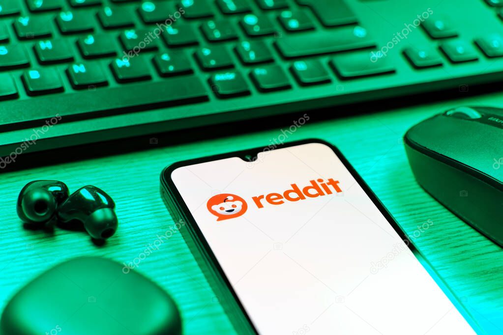 Prague, Czechia - 08 12 2025: A side view of a desk with a keyboard and a mobile phone displaying the Reddit logo. Reddit is a platform for discussion, news, and community content.