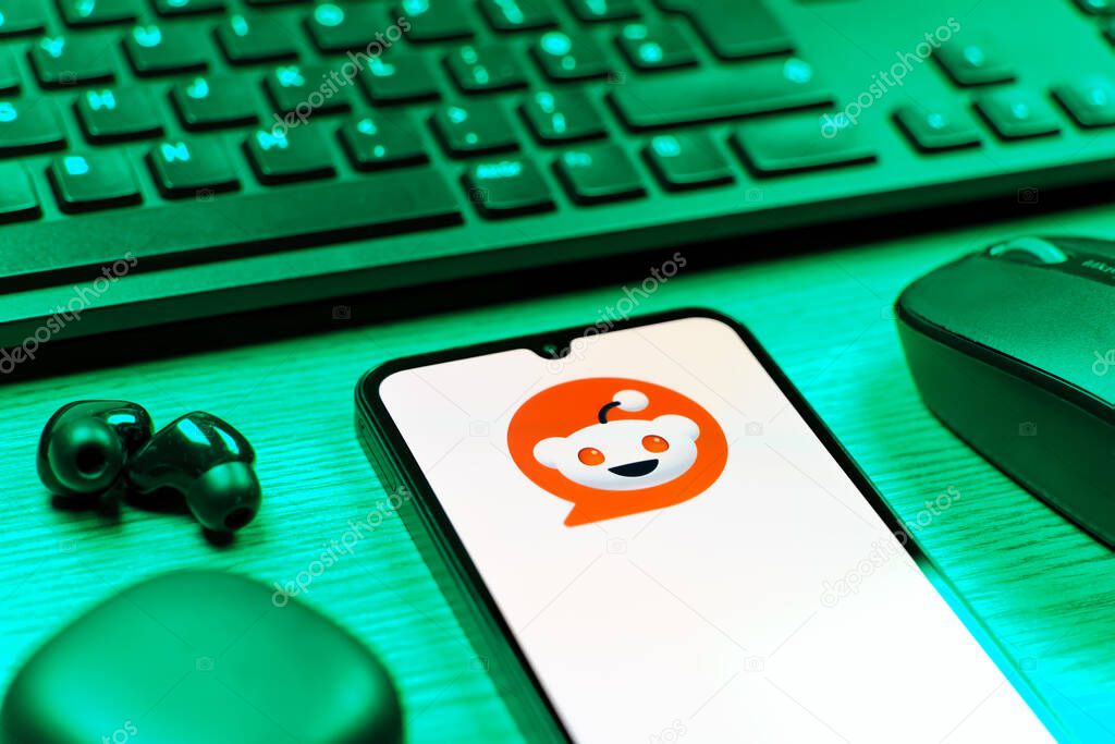 Prague, Czechia - 08 12 2025: A side view of a desk with a keyboard and a mobile phone displaying the Reddit logo. Reddit is a platform for discussion, news, and community content.