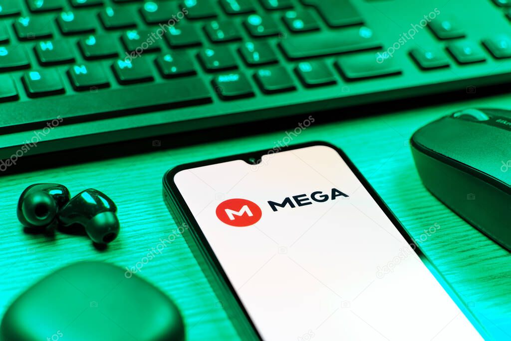 Prague, Czechia - 08 12 2025: A side view of a desk with a keyboard and a mobile phone displaying the Mega logo. Mega is a platform for cloud storage with encrypted file sharing.