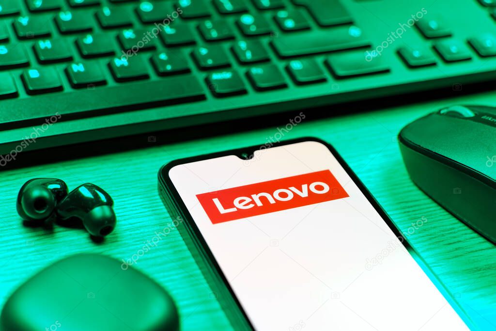 Prague, Czechia - 08 12 2025: A side view of a desk with a keyboard and a mobile phone displaying the Lenovo logo. Lenovo is a technology company producing computers and electronics.