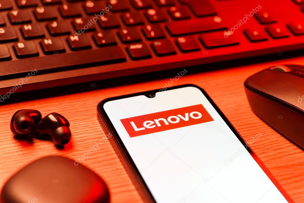 Prague, Czechia - 08 12 2025: A side view of a desk with a keyboard and a mobile phone displaying the Lenovo logo. Lenovo is a technology company producing computers and electronics.