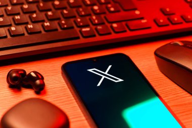 Prague, Czechia - 08 12 2025: A side view of a desk with a keyboard and a mobile phone displaying the X logo. X is a platform for sharing short posts and updates.