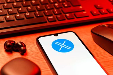 Prague, Czechia - 08 12 2025: A side view of a desk with a keyboard and a mobile phone displaying the X logo. X is a platform for sharing short posts and updates.