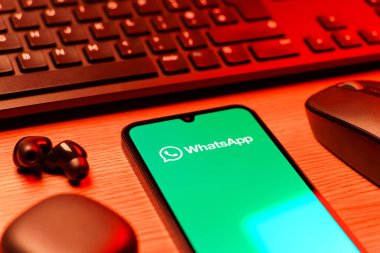 Prague, Czechia - 08 12 2025: A side view of a desk with a keyboard and a mobile phone displaying the WhatsApp logo. WhatsApp is an app for sending texts, calls, and media.